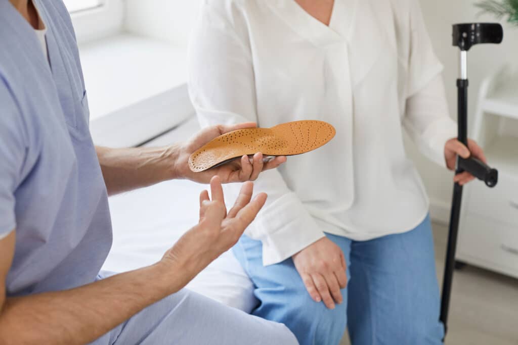 Doctor podiatrist gives medical orthotic insoles to a woman patient with a foot injury